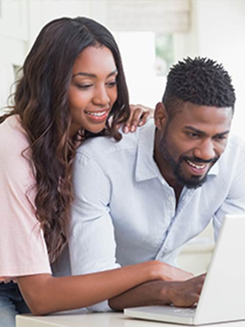 smiling woman and man at kitchen table on laptop filling out their online loan application